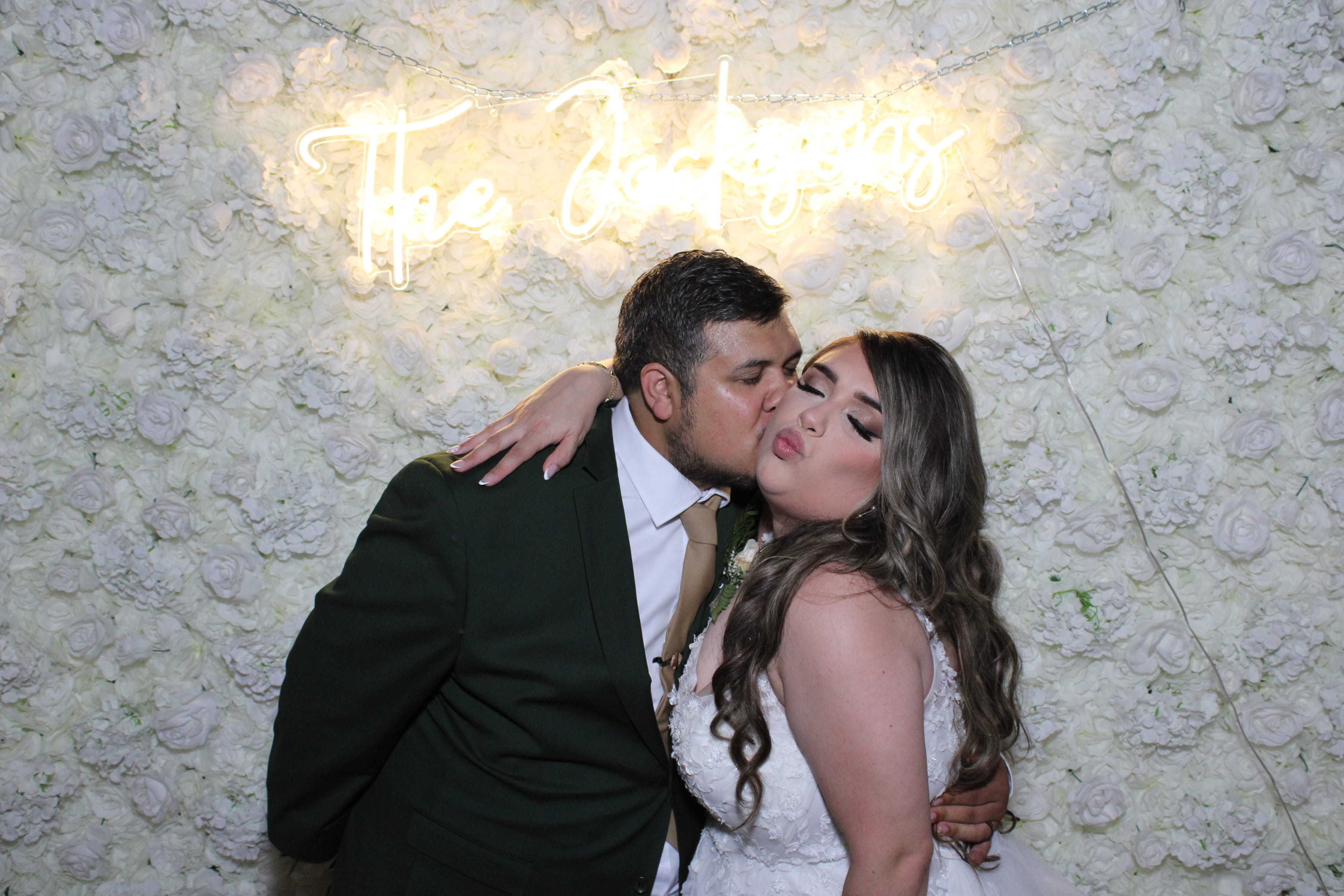 Wedding couple kissing in front of a neon 'The Jacksons' sign and white floral wall